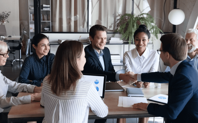 Foto de un grupo de empresarios, entre hombres y mujeres reunidos en la mesa de una oficina, dos de los hombres se dan la mano para hablar sobre los beneficios de la Transferencia Temporal  Valores.