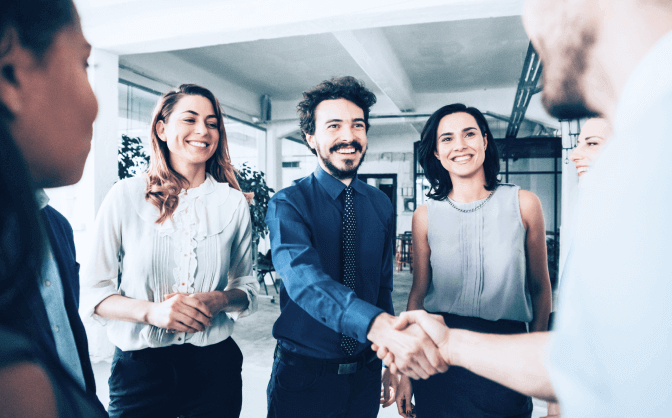 Foto de un grupo de personas reunidas sonriendo en la oficina, dos hombres se dan la mano y hablan sobre inversiones para obtener crecimiento de capital en Valores Bancolombia.