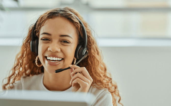 Foto de una mujer con cabello color cobrizo y con una diadema de call center, sonriendo mientras consulta en Valores Bancolombia su contacto para comunicarse de forma directa y clara con los asesores.