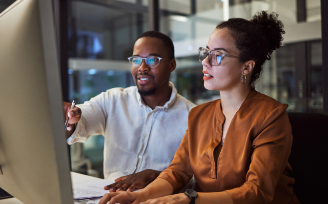 Foto de una mujer y un hombre con gafas revisando en el computador de la oficinas las inversiones internacionales de Valores Bancolombia.