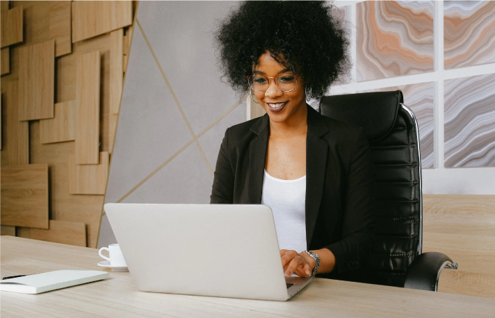 Foto de una mujer sonriendo mientras mira en su computador la página web de Valores Bancolombia para buscar información sobre los fondos de inversión